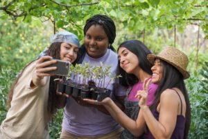 group of young women taking selfies while planting trees for Earth Month.