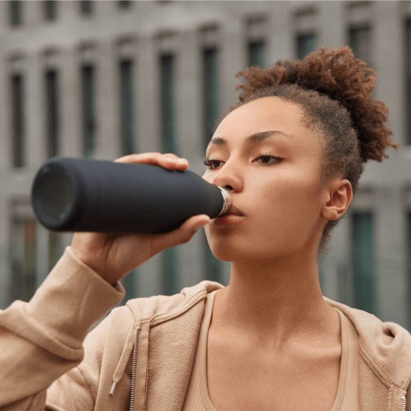 young woman drinking from reusable bottle